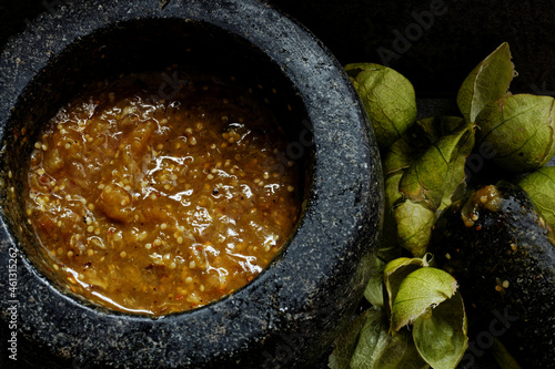 Roasted tomatillo salsa with toasted chilies de arbol in molcajete and tomatillo husks photo