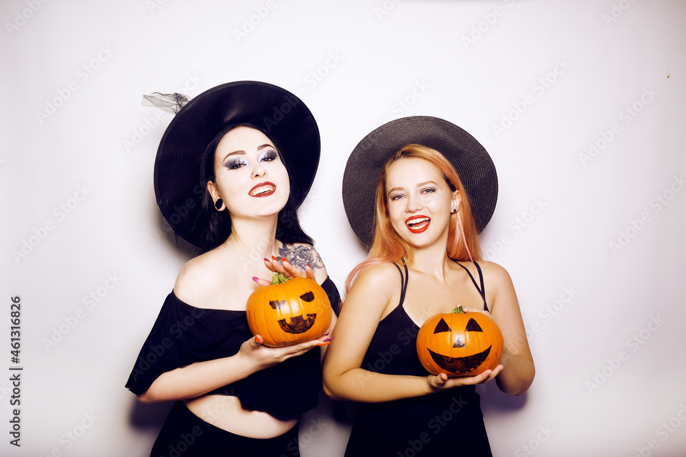 Two girls witches in hats are holding pumpkins in their hands and smiling for the camera, posing, dancing. Women celebrate Halloween, photo on white background Two girls witches in hats are holding pumpkins in their hands and smiling for the camera, posing, dancing. Women celebrate Halloween, photo on white background