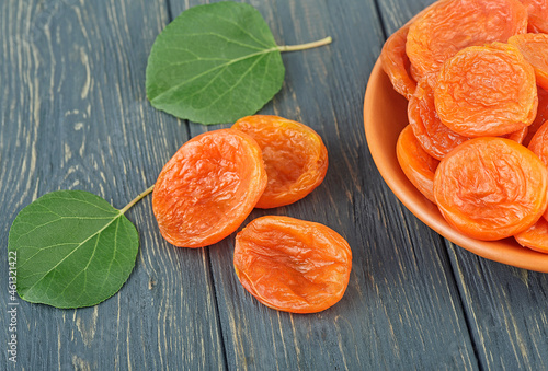 Dried apricots in bowl with green leaves on rustic wooden background