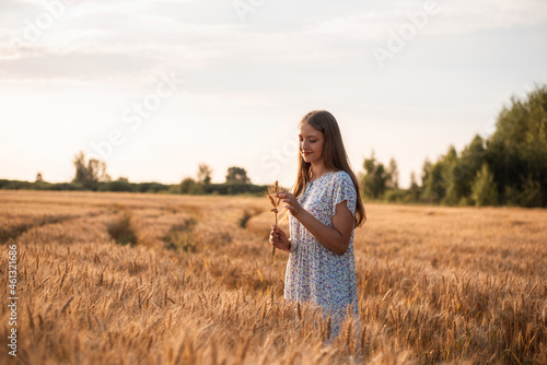 Portrait of young blond girl with some rye ears in her hands in field of rye at sunset. Lonely girl in field of rye