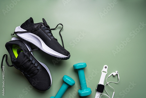 Flat lay sport with shoes, dumbbells, watch, and earphones on green background. Concept healthy lifestyle, sport and diet