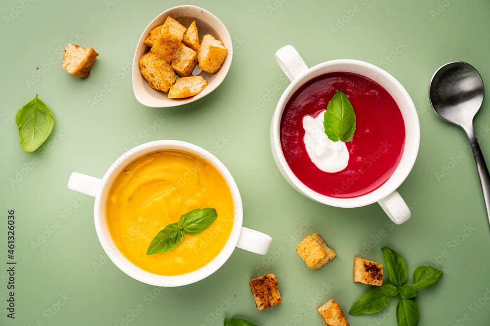 Vegetarian beetroot and pumpkin cream soups in a bowls with croutons on a green background, top view