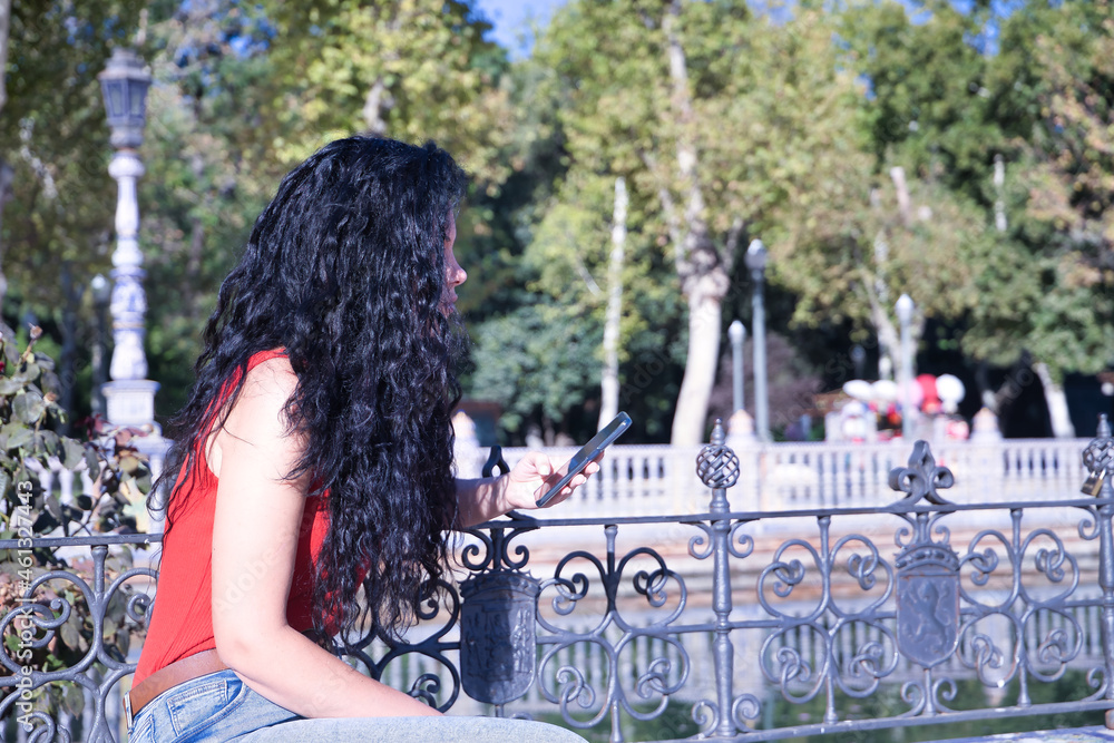 Middle-aged adult Hispanic woman with black curly hair checking social networks on her cell phone. Concept of technology and social networks.