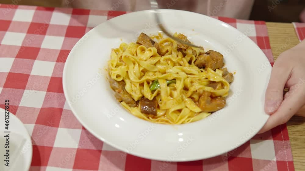 Top view of a woman eating a delicious hot pasta with pork medallions, cheese, sauce and trumpet mushrooms. Top view of a woman eating a delicious hot pasta with pork medallions, cheese, sauce and trumpet mushrooms.