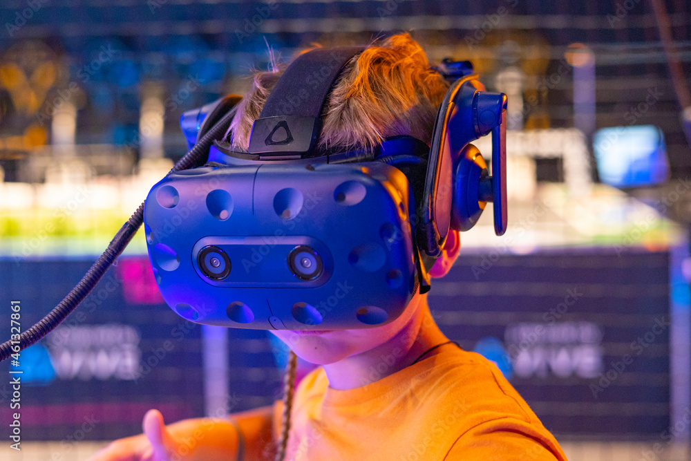 cute boy in virtual reality helmet and with controller in his hands plays online game in VR club, game simulates behavior in fictional world, gadgets and virtual reality addiction cute boy in virtual reality helmet and with controller in his hands plays online game in VR club, game simulates behavior in fictional world, gadgets and virtual reality addiction