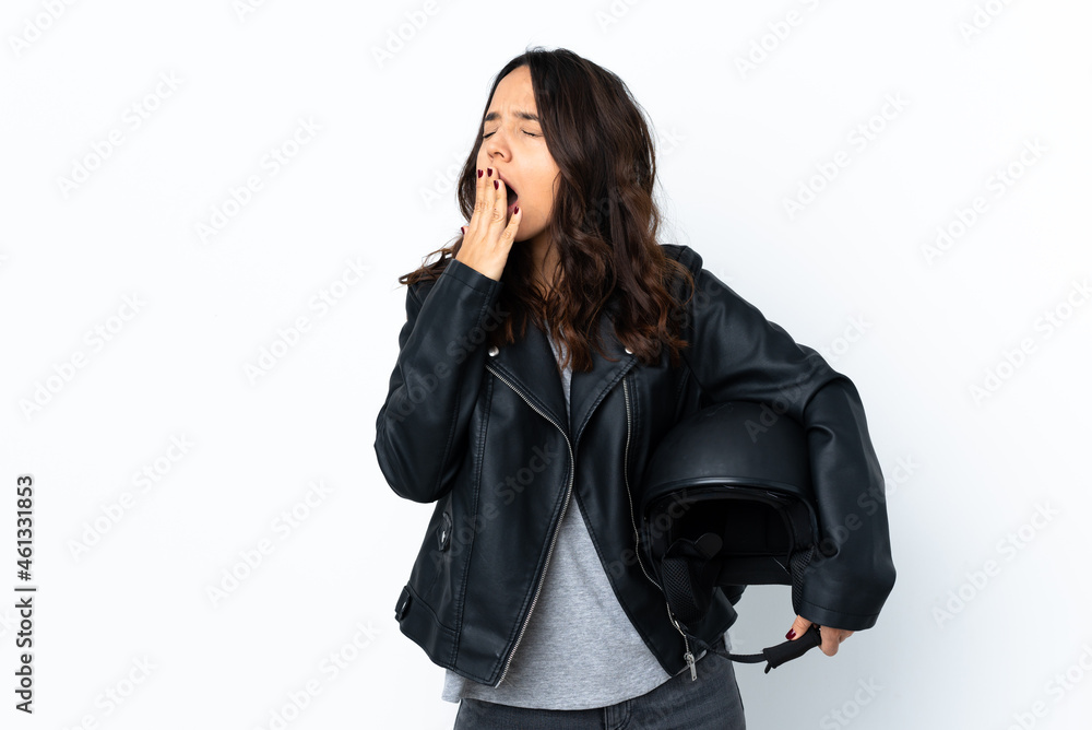 Young woman holding a motorcycle helmet over isolated white background yawning and covering wide open mouth with hand Young woman holding a motorcycle helmet over isolated white background yawning and covering wide open mouth with hand