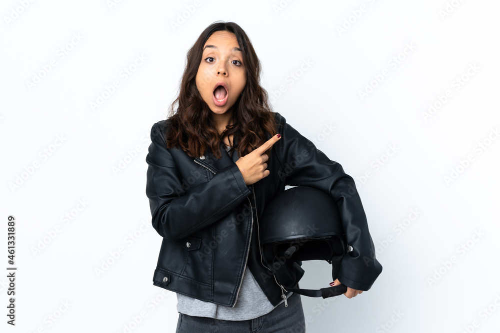 Young woman holding a motorcycle helmet over isolated white background surprised and pointing side Young woman holding a motorcycle helmet over isolated white background surprised and pointing side