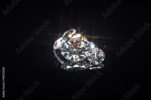 Diamonds selective focus on black reflective background. Polished gem stones of different size cuts. Light reflect as star shape ray burst, starburst or sunbeam. High quality brilliant jewel display.