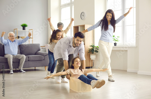 Happy family having fun at home. Cheerful mom, dad, grandma, grandpa and little children enjoying a good time together and playing with a plastic container in a new modern white living room interior