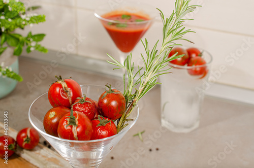 Fresh organic ripe red cherry tomatoes in the cocktail glass with branches of rosemary. Top view with blurred glass and texture background.