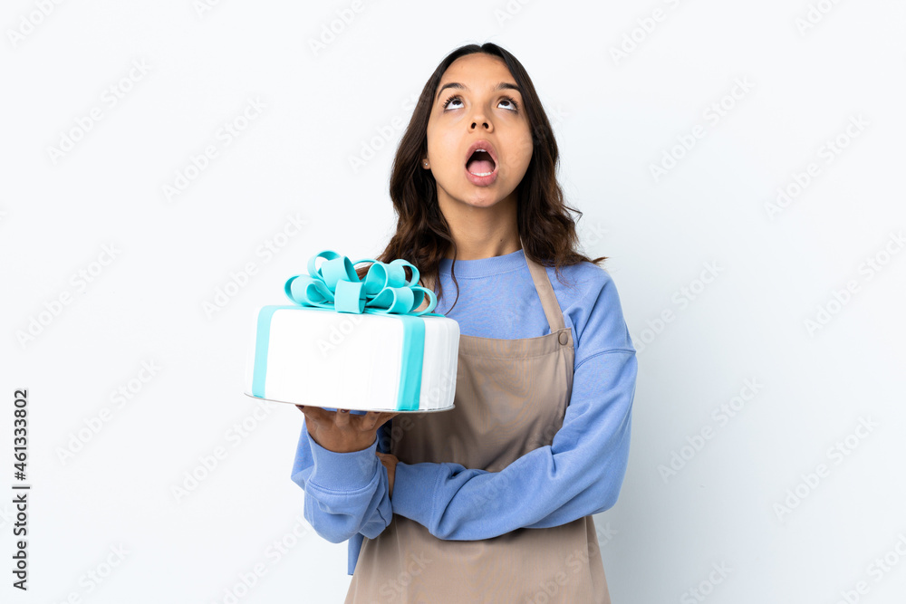 Pastry chef holding a big cake over isolated white background looking up and with surprised expression Pastry chef holding a big cake over isolated white background looking up and with surprised expression