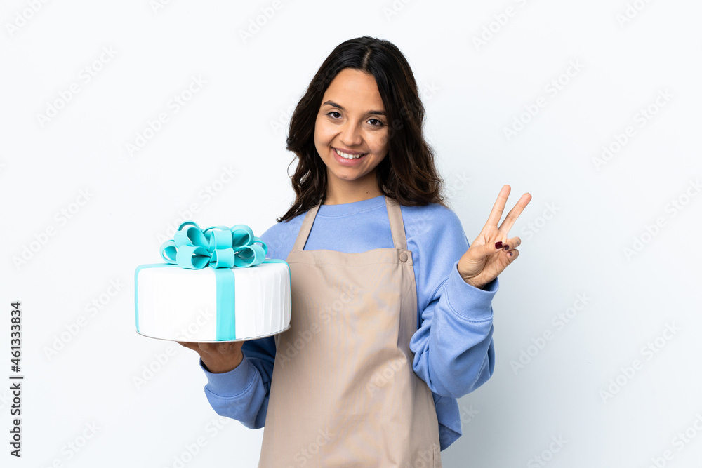 Pastry chef holding a big cake over isolated white background smiling and showing victory sign Pastry chef holding a big cake over isolated white background smiling and showing victory sign