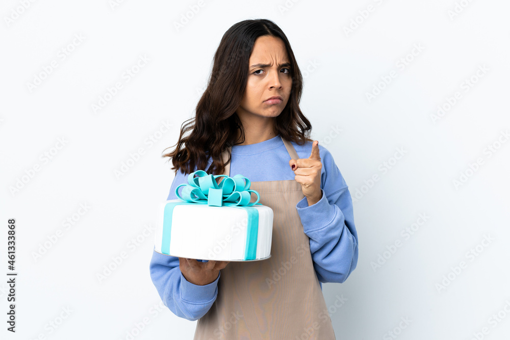 Pastry chef holding a big cake over isolated white background frustrated and pointing to the front Pastry chef holding a big cake over isolated white background frustrated and pointing to the front