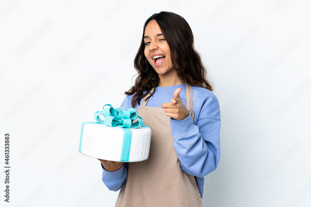 Pastry chef holding a big cake over isolated white background surprised and pointing front Pastry chef holding a big cake over isolated white background surprised and pointing front