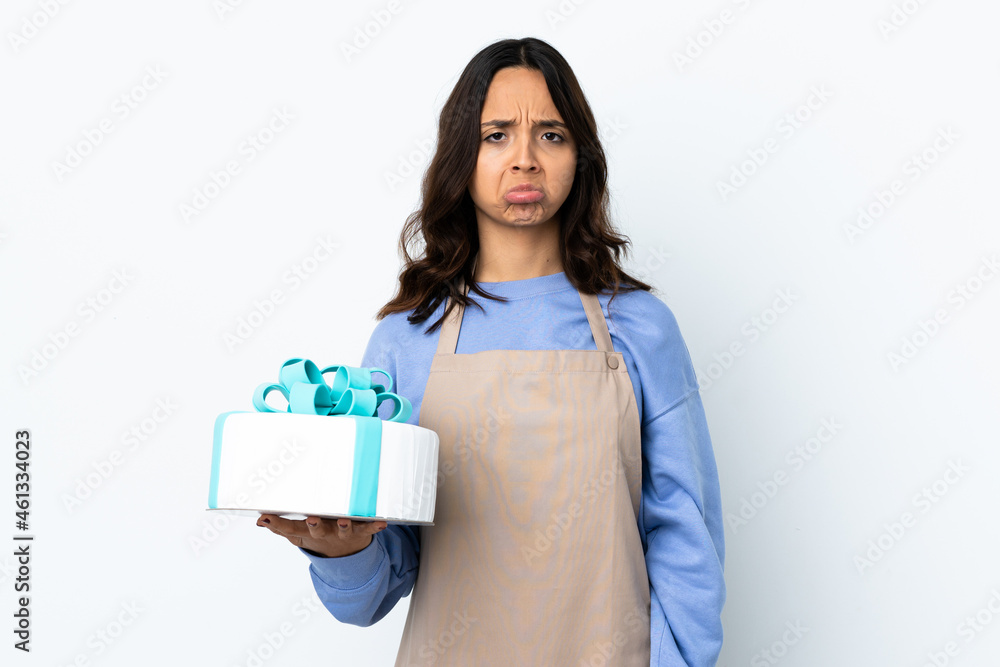 Pastry chef holding a big cake over isolated white background with sad expression Pastry chef holding a big cake over isolated white background with sad expression
