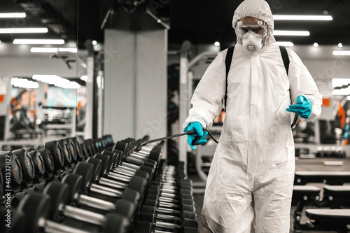 A worried and serious man carefully disinfects neatly stacked dumbbells in the gym of an indoor concept. COVID19 outbreak, keep social distance, coronavirus situation, pandemic, epidemic