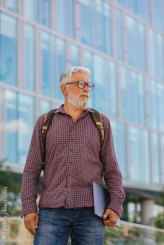 an adult gray-haired man with a beard goes to the office to work. a senior businessman in a shirt and with a laptop is making a career in a large company. a stylish European talks on the phone with an adult gray-haired man with a beard goes to the office to work. a senior businessman in a shirt and with a laptop is making a career in a large company. a stylish European talks on the phone with