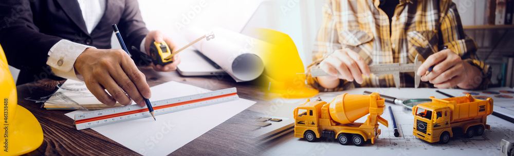 Fototapeta premium Two colleagues discussing data working and tablet, laptop with on on architectural project at construction site at desk in office