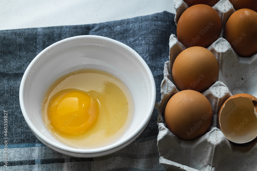 Top view of a plate with a broken egg near a chicken box on a gray napkin on the table. Top view of a plate with a broken egg near a chicken box on a gray napkin on the table.