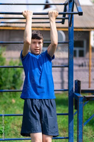 teenage boy exercising outdoors, sports ground in the yard, he pulls himself up on the horizontal bar, healthy lifestyle