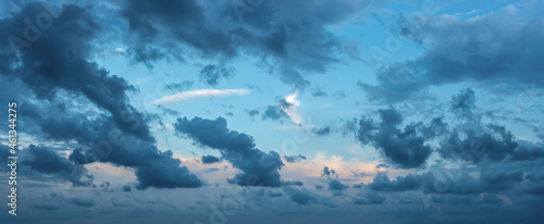 Blue stormy clouds blown by the strong wind across the sky at evening. Dramatic sky with torn dark clouds low over the horizon. Overcast skyscape panorama at blue hour. Wide windy weather cloudscape.