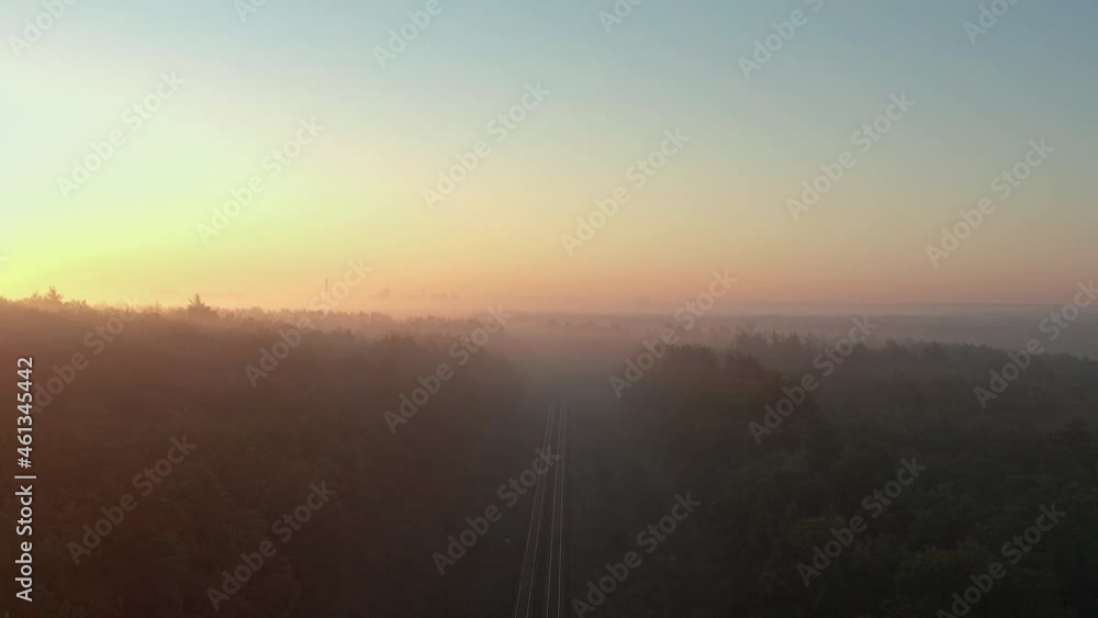 Aerial view of a foggy autumn forest with a railway road at sunrise with a silhouette of the city in the background. Aerial view of a foggy autumn forest with a railway road at sunrise with a silhouette of the city in the background.