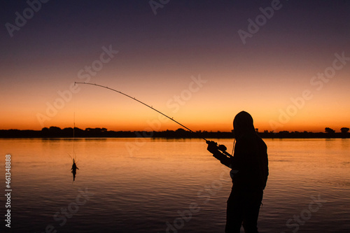 Silhouette of a man catching a fish with the sunset in the background.