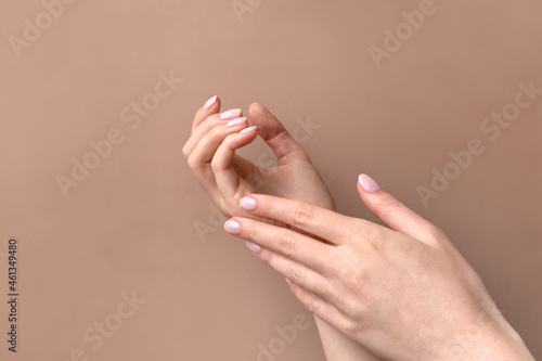 Beautiful woman s hands on beige background applying lotion or cream. Palms with natural pink manicure. Skincare. Soft clean hand concept.