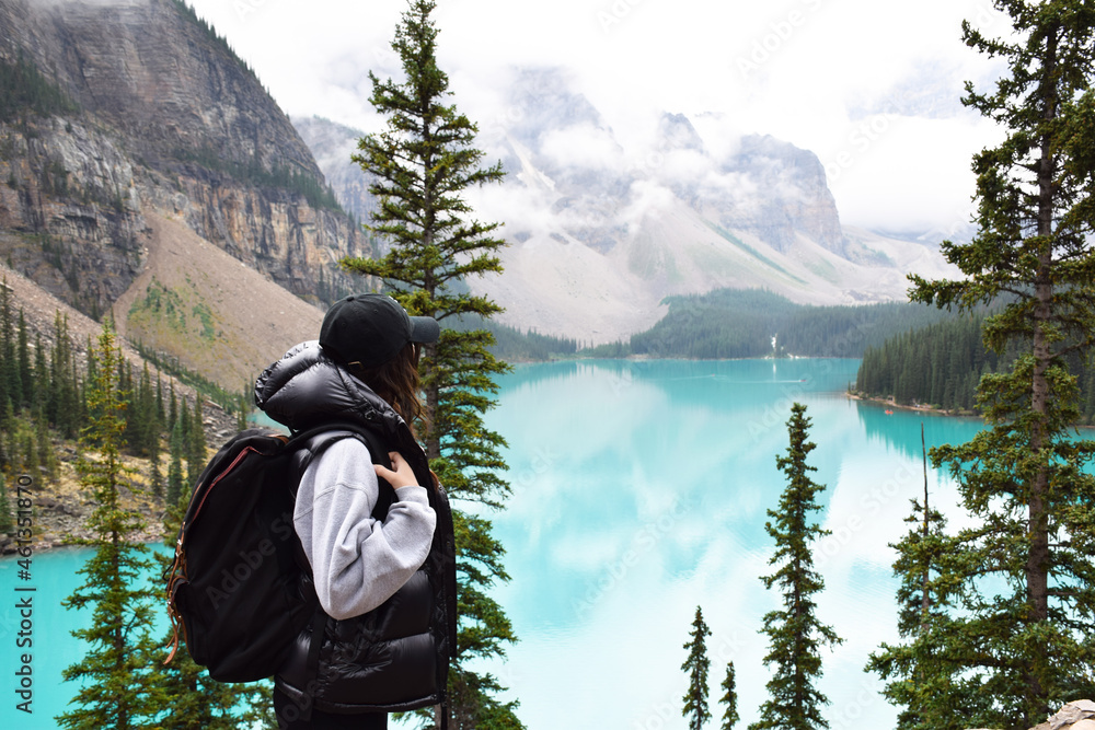 Young girl with backpack admiring the beauty of turquoise lake and mountains