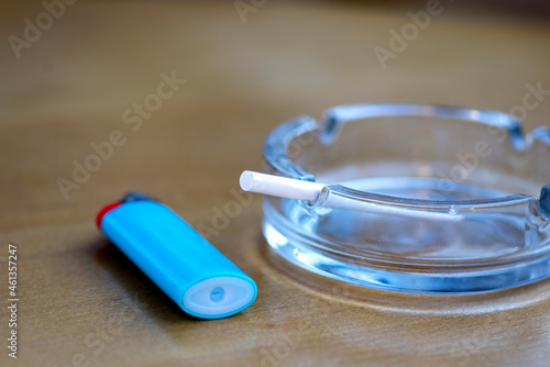 Glass ashtray with ligter on the woooden table.