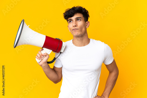 Young Argentinian man isolated on yellow background holding a megaphone and thinking
