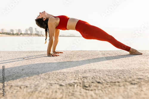 Adult woman practising yoga exercise by the sea at sunset - Athletic hispanic female doing purvottanasana position outdoors - Fitness, sport and healthy lifestyle concept photo