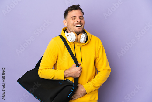 Young sport caucasian man with bag isolated purple background smiling a lot