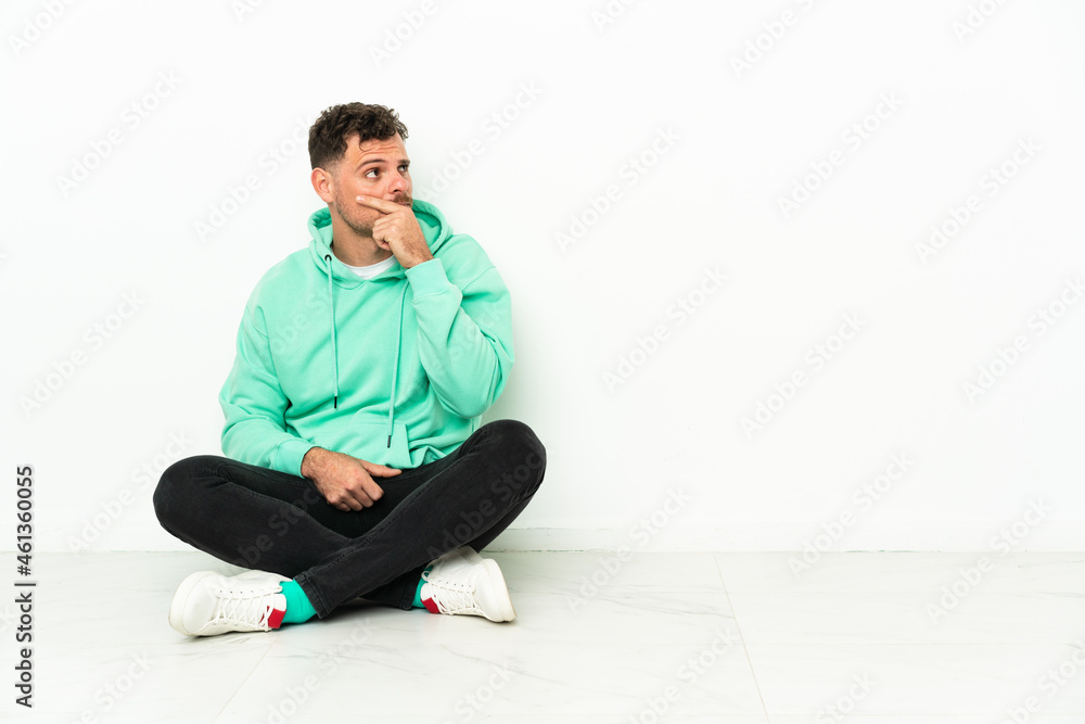 Young handsome caucasian man sitting on the floor having doubts and with confuse face expression Young handsome caucasian man sitting on the floor having doubts and with confuse face expression