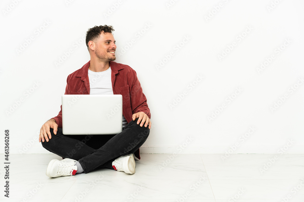 Young handsome caucasian man sit-in on the floor with laptop in lateral position Young handsome caucasian man sit-in on the floor with laptop in lateral position