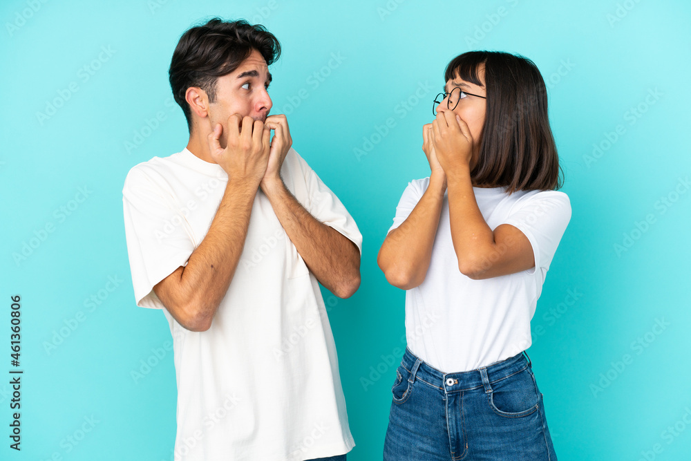 Young mixed race couple isolated on blue background is a little bit nervous and scared putting hands to mouth Young mixed race couple isolated on blue background is a little bit nervous and scared putting hands to mouth