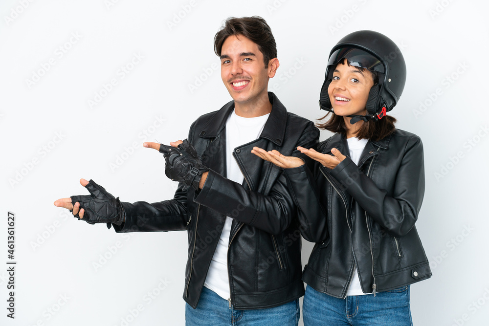 Young mixed race couple with a motorcycle helmet isolated on white background extending hands to the side for inviting to come Young mixed race couple with a motorcycle helmet isolated on white background extending hands to the side for inviting to come