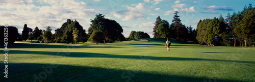 Panorama of back view of man walk across pristine golf course photo