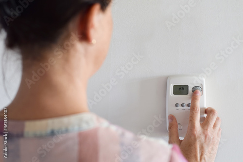 Woman is adjusting indoor thermostat settings of a home