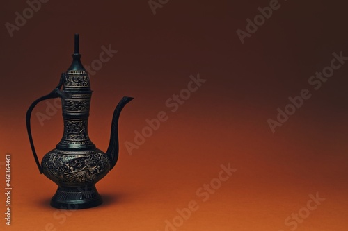 Vintage traditional islamic oriental engraved pitcher handmade on dark orange background. Elegant arabian antique tall metal jug,copy space. photo