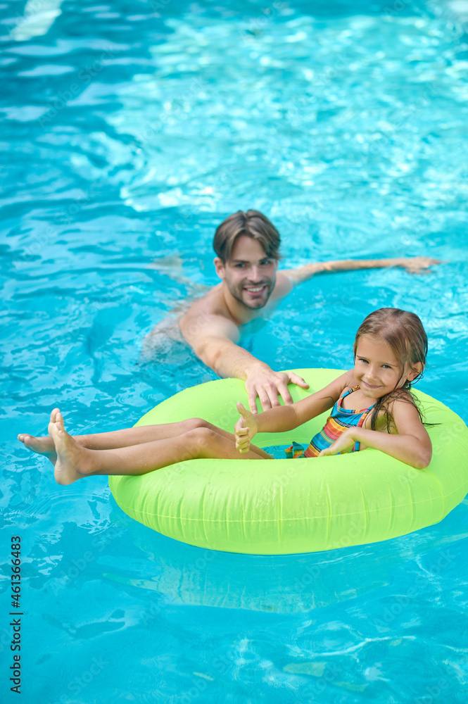 A young man and his daughter swimming in the pool and looking enjoyed