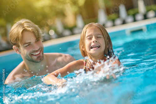 A young man and his kid swimming in the pool and looking enjoyed