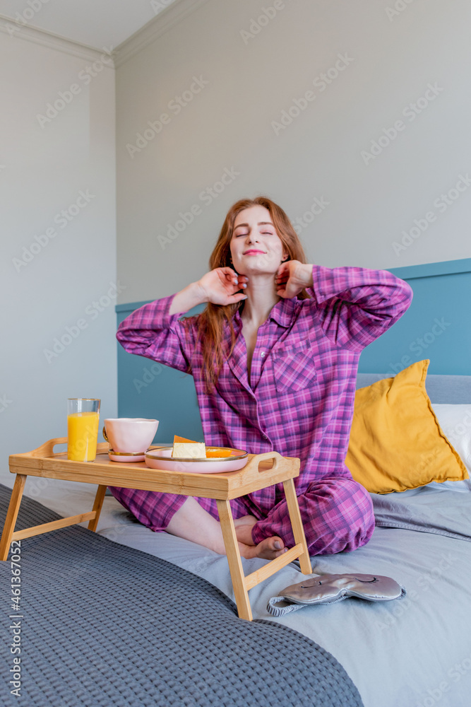 Young woman in pink pajamas has healthy breakfast while lying on bed in bedroom. Young woman in pink pajamas has healthy breakfast while lying on bed in bedroom.