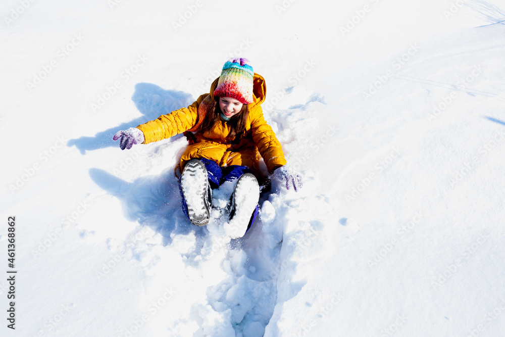 Girl in a yellow jacket is lying in the snow. Sunny snowy day for fun.