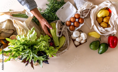 Adult woman pulls out the purchased products from farmers market from the fabric bags. Zero waste concept. Flat lay