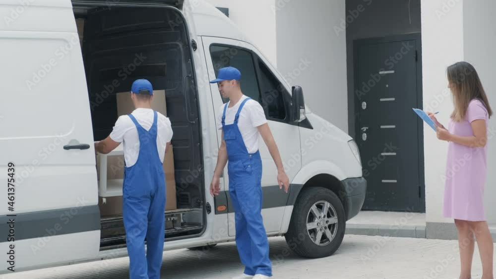 Two young workers of removal company are loading boxes and furniture into a minibus Two young workers of removal company are loading boxes and furniture into a minibus