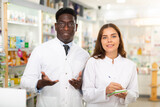 Portrait of two positive pharmacists in a pharmacy, standing in the sales hall and making working notes