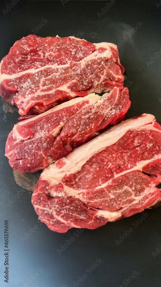 Roasting meat for dinner or lunch. Classic selected beef steak. Two pieces of juicy pork on a black background. Cooking meat in a pan at home. The benefits of protein products for humans.