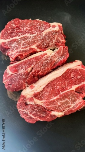 Roasting meat for dinner or lunch. Classic selected beef steak. Two pieces of juicy pork on a black background. Cooking meat in a pan at home. The benefits of protein products for humans.