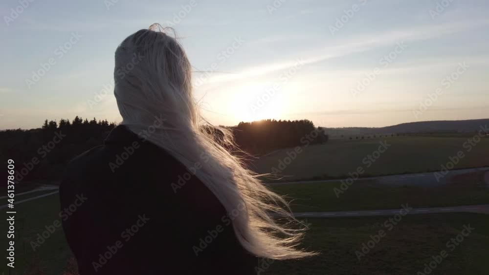 Woman with long hair blowing in the wind watching the sunset panorama from the hill in autumn Woman with long hair blowing in the wind watching the sunset panorama from the hill in autumn